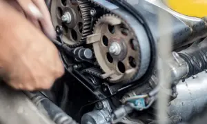 Mano che lavora per cambiare cinghia distribuzione motore auto, con ingranaggi e pulegge in primo piano.