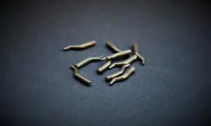 Metalowe pozycjonery haczyka, drobne akcesoria wędkarskie, leżą na ciemnym tle.