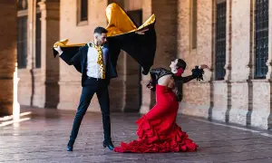 Pareja bailando flamenco con pasión. Él, con capa negra y dorada, ella, con vestido rojo voluminoso. Puro jaleo flamenco.