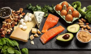 Na talerzu składniki na dietę keto: łosoś, awokado, jajka, sery, orzechy, brokuły i szpinak.
