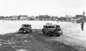 Snöig vinterdag med flera 70 tals bilar redo för race. En åskådare står vid sidan av banan.