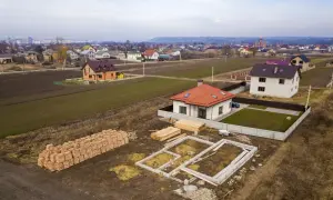 Działka inwestycyjna a budowlana: widać fundamenty domu, sterty cegieł i drewna, gotowe domy i pola uprawne w tle.