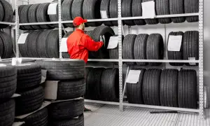 Pracownik w czerwonym kombinezonie przegląda opony na regałach. W magazynie panuje porządek, a opony są ułożone w rzędach. To idealne miejsce dla miłośników motoryzacji, którzy szukają części do swoich pojazdów.