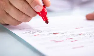 Mano con pennarello rosso che evidenzia testo su foglio, illustrando la differenza tra iscrizione e trascrizione.