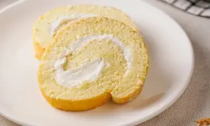 Zwei Scheiben einer saftigen Zitronenrolle mit cremiger Füllung auf einem weißen Teller. Ein köstliches Zitronenrolle Rezept zum Nachbacken.