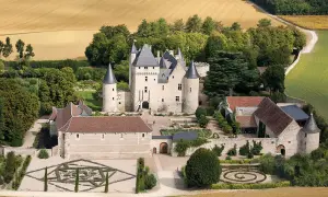 Vue aérienne du **château du Riveau**, un édifice médiéval entouré de jardins à la française et de champs dorés.