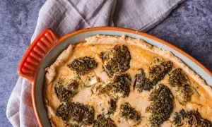 En gyllene ost och broccolipaj i en orange kantig form, redo att serveras.