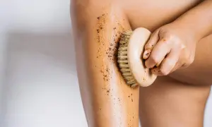 Mano che applica fango dimagrante con spazzola su gamba. Esfoliazione e benessere per la pelle.
