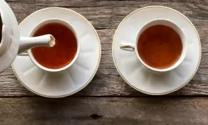 Dwie filiżanki z herbatą pu erh, z których jedna jest nalewana z czajniczka. Napój ma głęboki, bursztynowy kolor, a jego właściwości zdrowotne są cenione od wieków.