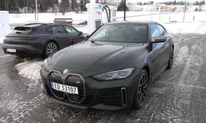 Zielone BMW i4 na ładowarce w zimowy dzień. Obok stoi ciemny Porsche Taycan.
