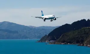 Samolot Air New Zealand ląduje nad turkusową wodą, zbliżając się do wybrzeża. Zastanawiasz się, ile kosztuje lot do Nowej Zelandii?