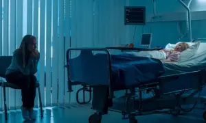 Zmartwiona matka siedzi obok śpiącego dziecka w szpitalnym łóżku, co może sugerować zespół Münchhausena u matek.