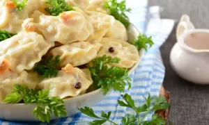 Pyszne pierogi z ziemniakami, udekorowane natką pietruszki i ziarnami pieprzu, czekają na talerzu.