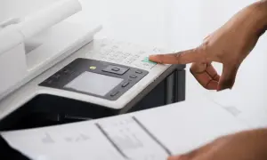 Dłoń naciska zielony przycisk na drukarce, która drukuje na różowo.