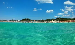 Acque cristalline e una spiaggia affollata a Porto Cesareo, con ombrelloni colorati e gente che si gode il sole. Lu specchia Porto Cesareo, un paradiso estivo.