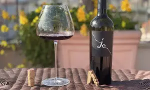 Un calice di vino rosso e una bottiglia di Negroamaro Puglia, con tappo e cavatappi, su un tavolo all'aperto.