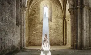 Cristina Vatielli, vestita di bianco, in piedi sotto un raggio di luce in un'antica abbazia.