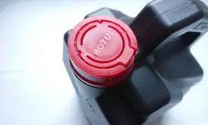 Czarne opakowanie oleju Motul z czerwoną zakrętką z logo.