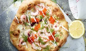En läcker pizza med räkor och mozzarella, toppad med rom och dill. En citronskiva ligger bredvid.