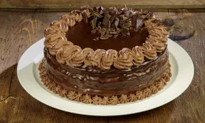 Torta compleanno cioccolato e panna, ricoperta di glassa lucida e decorata con riccioli di panna e scaglie di cioccolato.