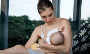 Delikatny moment karmienia piersią. Mama z miłością patrzy na swoje dziecko, które pije mleko z piersi.