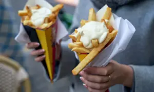Dwie porcje frytek w papierowych rożkach, polane gęstym, białym sosem.
