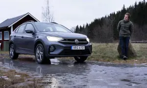 Grå VW Taigo står på en isig väg nära en röd stuga. En man står lutad mot en sten i bakgrunden.