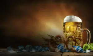 Boccale di birra dorata con schiuma abbondante, brezel e nastri a scacchi bianchi e blu, perfetti per le birre dell'Oktoberfest.