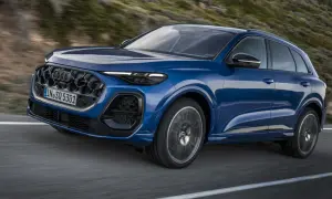 Niebieskie, nowe Audi Q5 z charakterystycznym grillem i ostrymi światłami pędzi po krętej drodze wśród wzgórz.