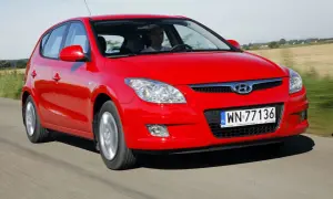 Czerwony Hyundai i30 1.6 CRDi jedzie po drodze wśród pól.