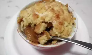Un delizioso crumble di mele appena sfornato, con la crosta dorata e il ripieno succoso. Una forchetta è immersa nel dolce.