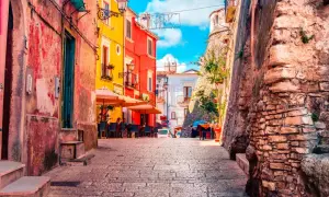 Vico del Gargano, Vicolo del Bacio: un vicolo pittoresco con case colorate, tavolini all'aperto e un'antica muraglia di pietra.