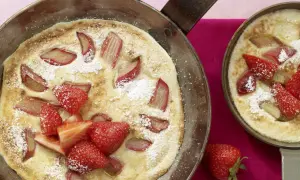 Zwei Pfannen mit frisch gebackenen Rhabarber-Pfannkuchen, garniert mit Erdbeeren und Puderzucker.