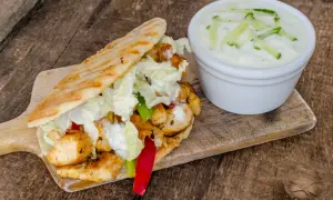 Gyros z kurczakiem, warzywami i sosem tzatziki na desce drewnianej.