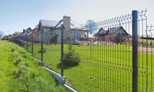 Solidne ogrodzenie antywłamaniowe chroni posesję z domami i zadbanym trawnikiem.
