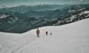 Trois alpinistes progressent sur un glacier enneigé, le Mont Rose en toile de fond. L'ascension est spectaculaire.