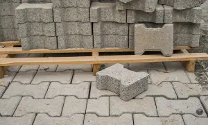 Stos kostki brukowej na palecie i pojedyncze elementy na ułożonej nawierzchni.