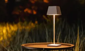 Nowoczesna lampa na balkon, stojąca na stoliku, oświetla wieczorny ogród.