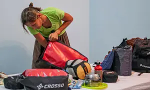 Kobieta pakuje sprzęt do sakw rowerowych. Na stole leżą torby, śpiwór, menażka i butla z gazem.