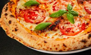 Zbliżenie na idealną pizzę z pomidorami, serem i bazylią, z przypieczonymi brzegami.