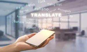 Dłoń trzyma smartfon, nad którym unosi się napis "TRANSLATE" otoczony nazwami języków. To pokazuje, jak przetłumaczyć tekst na wiele sposobów.