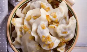Pierogi chłopskie z podsmażoną cebulką w glinianej misce.