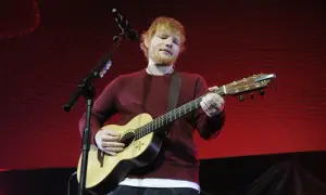 Ed Sheeran gra na gitarze akustycznej na tle czerwonej sceny.
