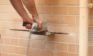 Ręce majstra tną ceglaną ścianę, przygotowując miejsce pod nadproże stalowe.