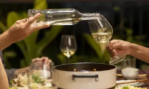 Hälla upp vitt vin till en måltid med tomatsås. En flaska hälls i ett glas, med en gryta och mat i bakgrunden.