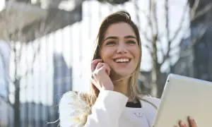 Donna sorridente con tablet, forse sta per uscire prima dal lavoro senza permesso, con un'aria di gioia e libertà.