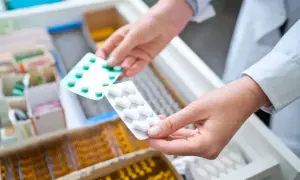 Farmaceuta wybiera leki z szuflady. W rękach trzyma opakowania z tabletkami, być może metotreksat, przygotowując je dla pacjenta.