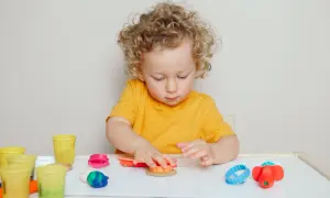 Chłopiec z kręconymi włosami bawi się plasteliną, co może być częścią terapii wspierającej diagnozę aspergera u dzieci.