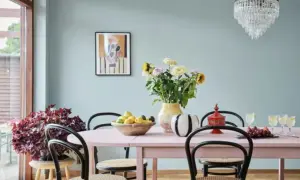 En matplats med ljusrosa bord, blommor i en gul vas och en skål med frukt. Kanske någon har valt att måla glasvasen för att få den att passa in.