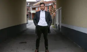 Mężczyzna w eleganckim płaszczu i białym golfie, dumnie prezentuje swoje stylowe sztruksy.
